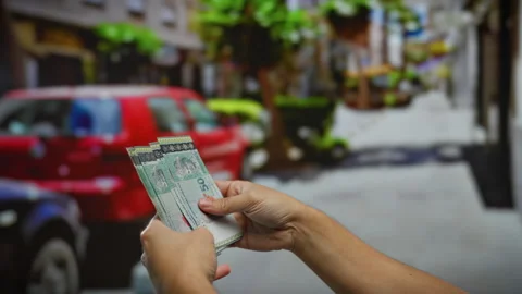 Man holding malaysian ringgit in an urban street setting with blurred cars .. Stock Footage 304952777