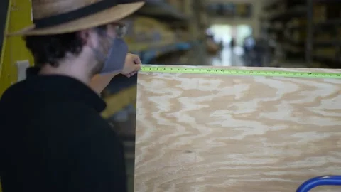 Man holding measuring tape on sheet of plywood in big box hardware store. 스톡 동영상 158378695
