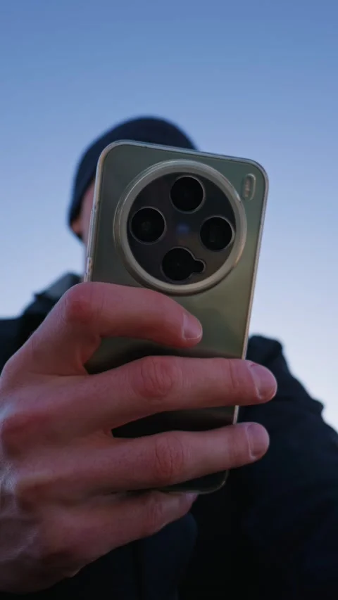 Man Holding Modern Smartphone With Large Camera Module Against Blue Sky Stock Footage 331143357