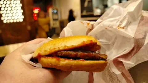 Man holding newly opened cheapest burger in front of fast food establishment Stock Footage 310854880