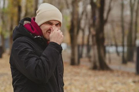 Man holding nose while walking in a park during autumn season, surrounded b.. Stock Photos