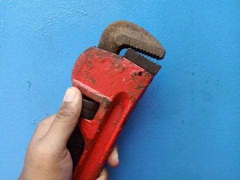 A man holding an old rusty pipe wrench without gloves on a blue background Foto stock