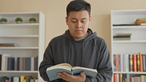 Man holding open book and turning a page amid bookshelves in a study buildi.. Stock Footage 337356223