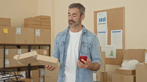 Man holding open parcel and checking smartphone in a building packing room;.. Stock Footage 339170018