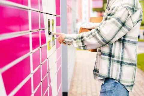 Man holding packages using an automated pink parcel locker terminal. Contac.. Stock Photos