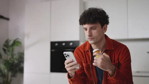 Man holding pill bottle while researching medication side effects on smartphone Stock Footage 337907738