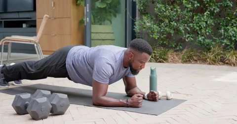 Man holding plank lowering resting wiping sweat returning on patio near weights Stock Footage 341665646