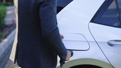 Man holding power supply cable at electric vehicle charging station. Hansome guy Stock Footage 249924366