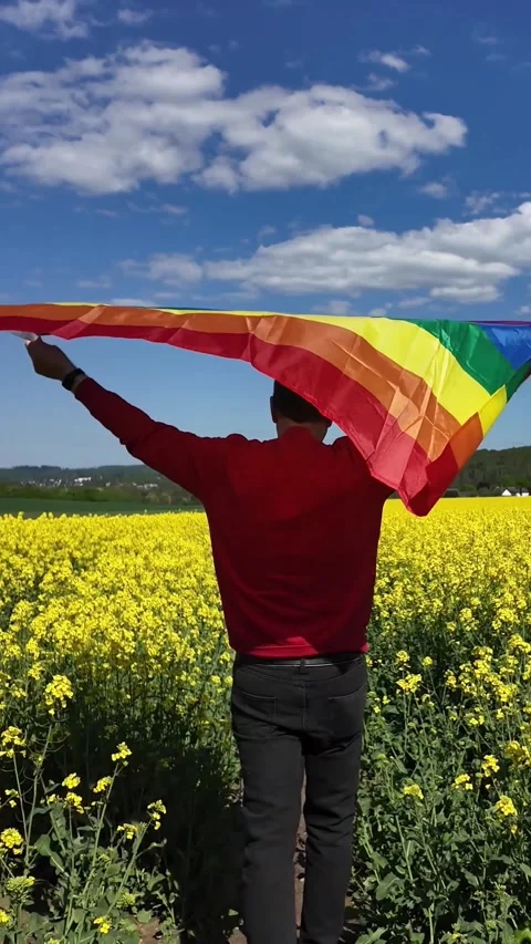 Man holding a pride flag in a yellow rapeseed field 動画素材 335015324