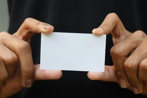 Man holding a rectangular white blank card between fingers on black backgroun Foto stock