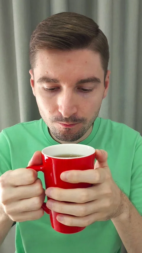 Man holding a red mug with both hands and sips a tea or coffee. Vertical shot Stock Footage 284042763