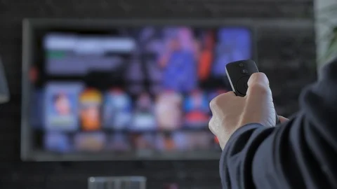 Man holding a remote control and searching for streaming media to play Stock Footage 103473158