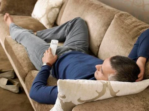 Man Holding Remote Control While Lying On Sofa Stock Photos