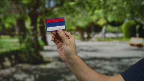 Man holding russian flag patch outdoors in a sunny park setting, showcasing.. Stock Footage 313911312