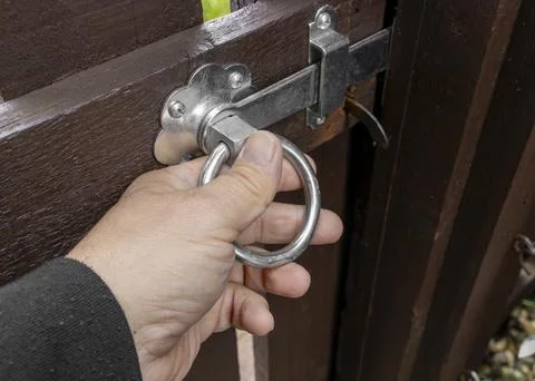 Man holding silver gate latch with a ring handle on brown wooden gate Foto stock