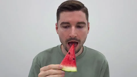 Man holding a slice of watermelon then takes a bit of red watermelon Video stock 284043862