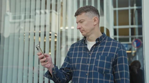 Man holding smartphone and looking at screen on street, standing by a store.. Stock Footage 339178338