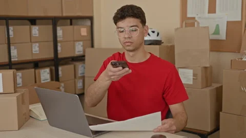 Man holding smartphone and reading a paper near laptop amid stacked boxes i.. Stock Footage 337376474