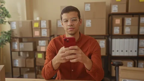 Man holding smartphone and smiling amid stacked shipping boxes at a small b.. Stock Footage 337376515
