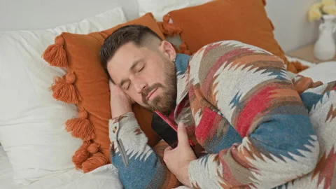 Man holding smartphone and tapping screen while nudging sleeping partner on.. 스톡 동영상 339218229