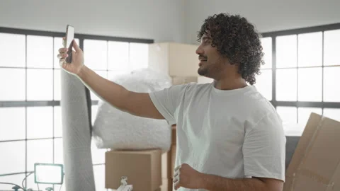 Man holding smartphone at arm taking a selfie in building with moving boxes.. Stock Footage 337404344