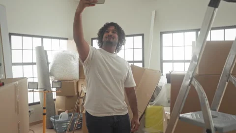 Man holding smartphone checks screen and takes a selfie among moving boxes .. Stock Footage 337399486