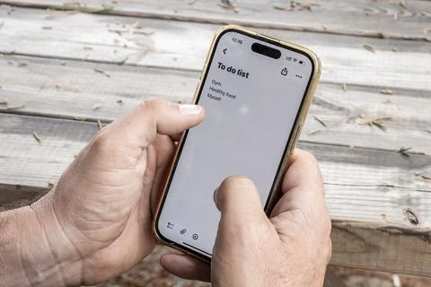 Man holding smartphone displaying a to-do list in a notes app while sitting.. Stock Photos