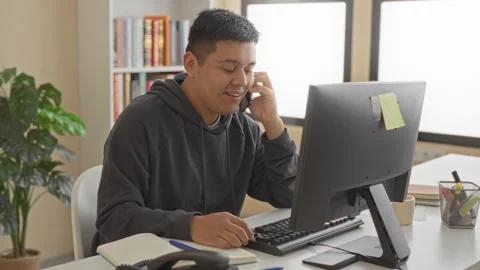 Man holding smartphone to ear and typing on desktop computer at office desk.. Stock Footage 337356067