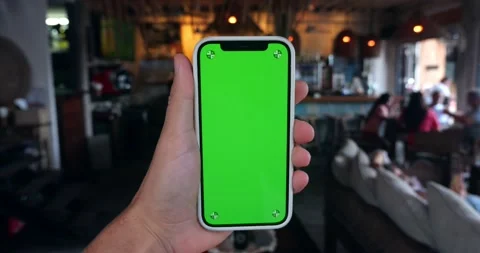 Man holding smartphone with green screen chroma key indoors at cafe or Stock Footage 219908707