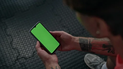 Man Holding Smartphone with Green Screen for Fitness App in Gym Stock Footage 345204436