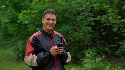 Man holding smartphone looking at camera in forest Video stock 158143860