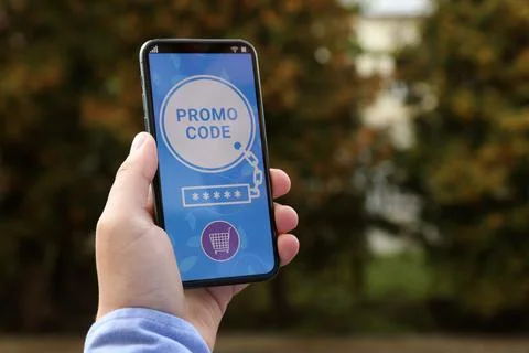 Man holding smartphone with promo code near trees outdoors, closeup. Space .. Stock Photos