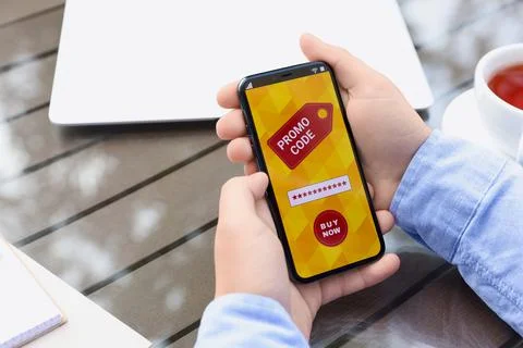 Man holding smartphone with promo code at wooden table outdoors, closeup Stock Photos