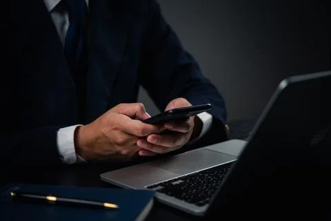 Man holding a smartphone while typing on a laptop keyboard in an office or .. Stock Photos