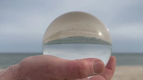 Man holding sphere lens on Beach during cloudy day. 4K Stock Footage 239197228