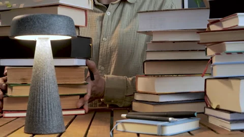Man holding stack of books on desk with lamp education concept Видео 334326012