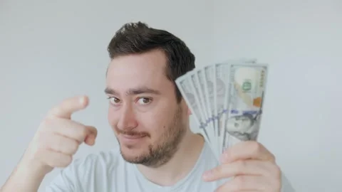 Man holding stack of cash while pointing directly at the camera in bright room Stock Footage 306260103