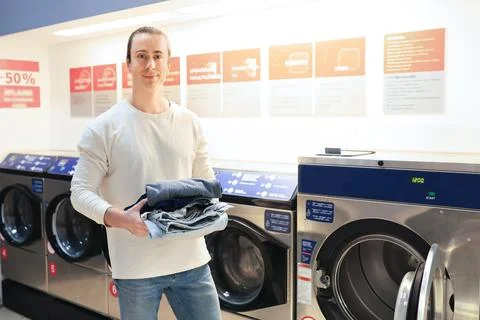 Man holding stack of clean clothes in self-service laundromat with washing .. Stock Photos