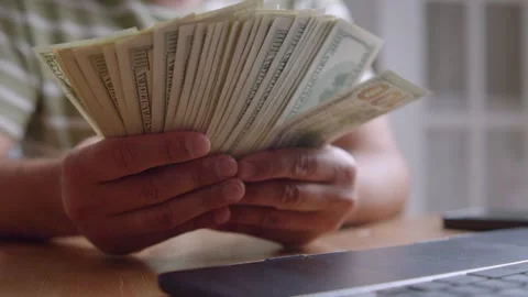Man Holding Stack Dollar Bills While Sitting At Wooden Table In Cozy Living Room Video stock 315355694
