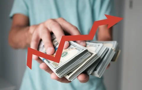 A man is holding a stack of money with a red arrow pointing downward Stock Photos