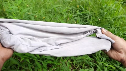 Man holding stretched gray pants on green grass background Stock Footage 296417056