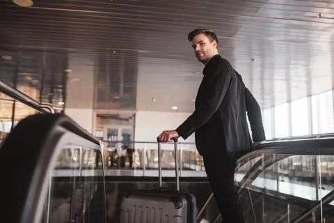 Man holding the suitcase and using the escalator Stock Photos