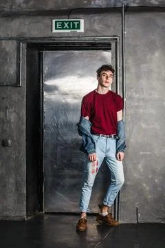 Man holding sunglasses while standing near metallic door, looking at camera with Stockfoto's