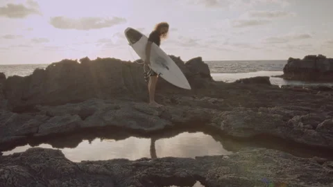 Man holding a surfboard while standing on rocks by the ocean Stock Footage 275165871