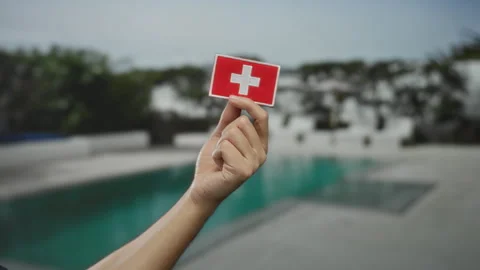 Man holding swiss flag patch above outdoor pool in a resort hotel setting, .. Stock Footage 314681262