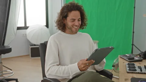 Man holding tablet and tapping screen, smiling while seated in studio with .. Stock Footage 337377102