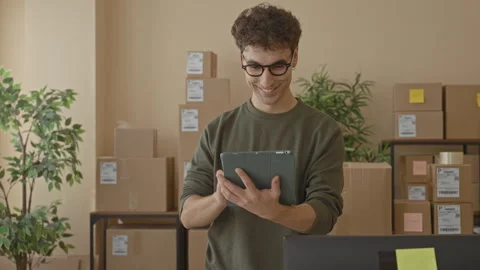Man holding tablet, hands visible, tapping screen amid stacked cardboard pa.. Stockbeeldmateriaal 337435425