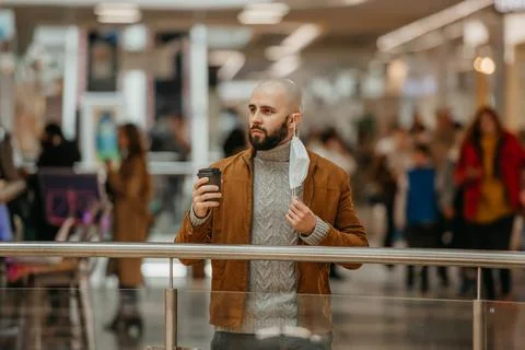 A man is holding a took-off mask while drinking coffee in the shopping center Stock Photos