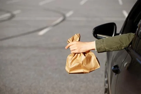 Man holding trash paper bag in hand out of window driving in car. Throwing ga Stock Photos