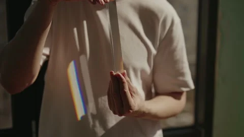 Man holding triangular glass prism, refracting sunlight and creating rainbow Stock Footage 312353344